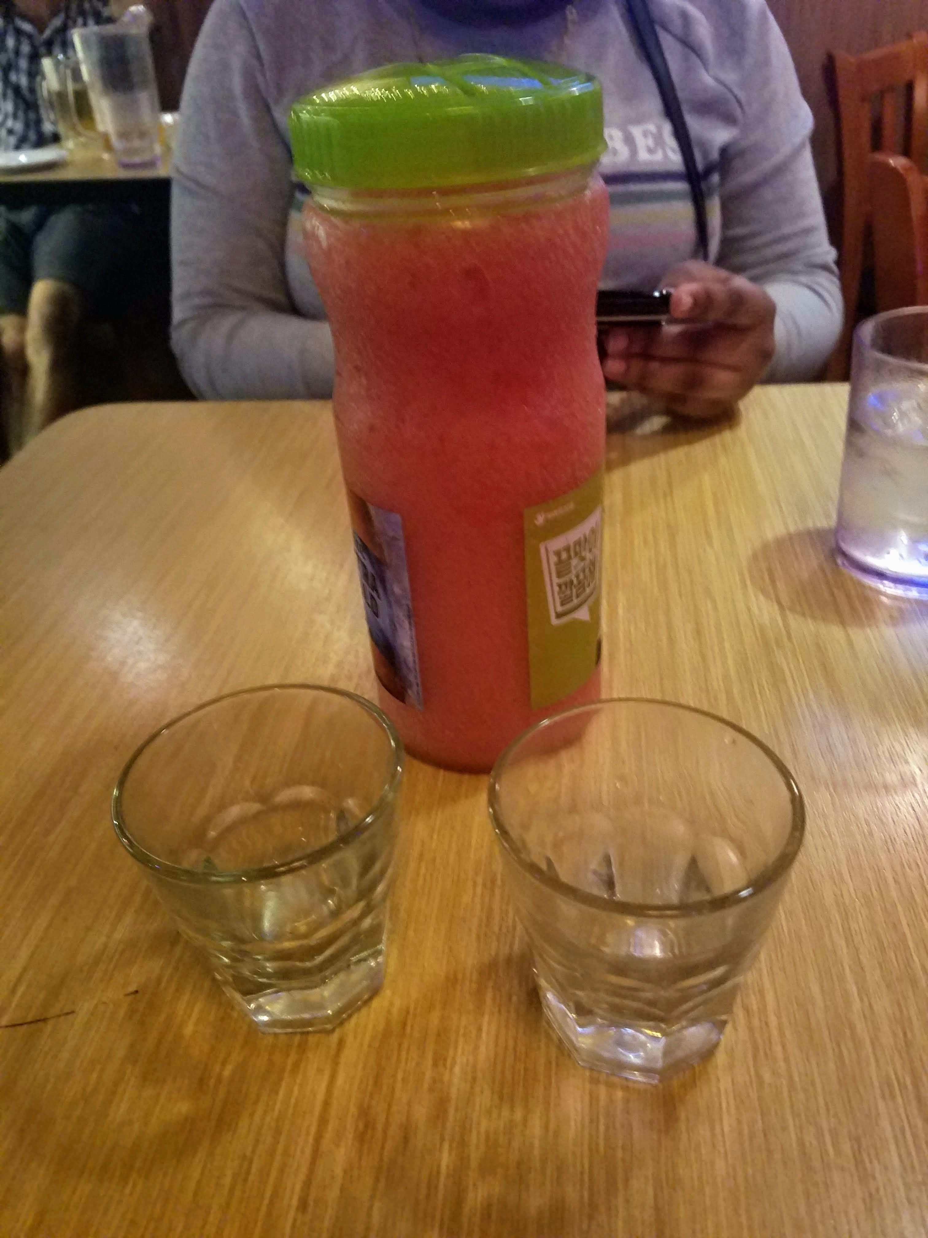 a plastic bottle filled with strawberry soju slushy. two empty shot glasses ready to be filled.