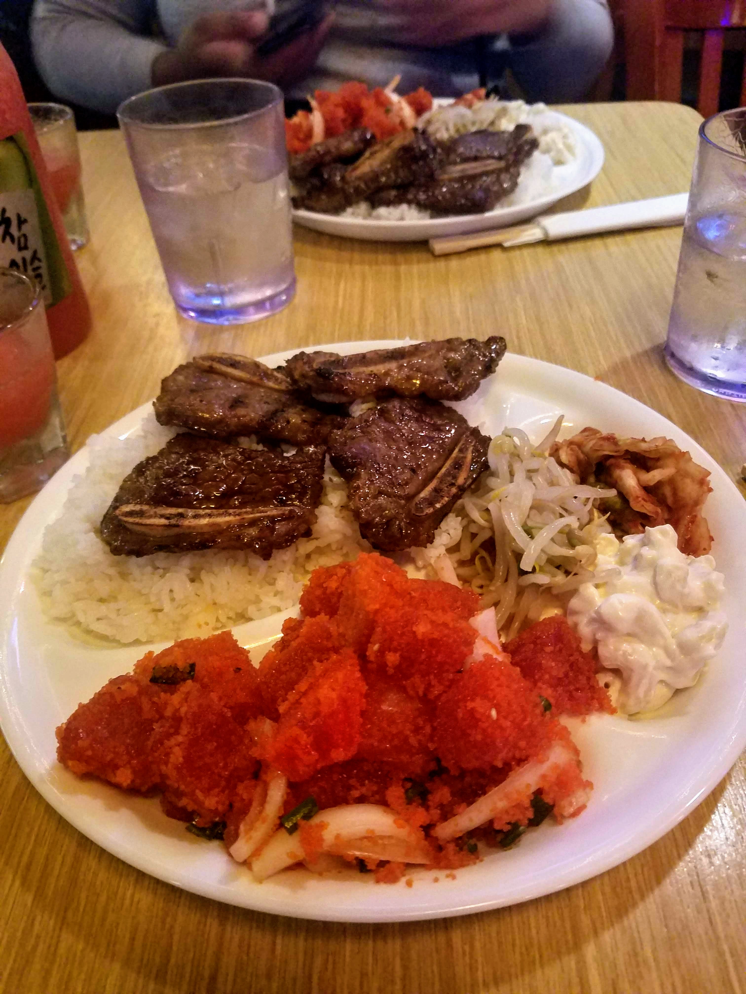 a cafeteria style plate with kalbi over rice, poke, and kimchi, bean sprouts, and macaroni salad.