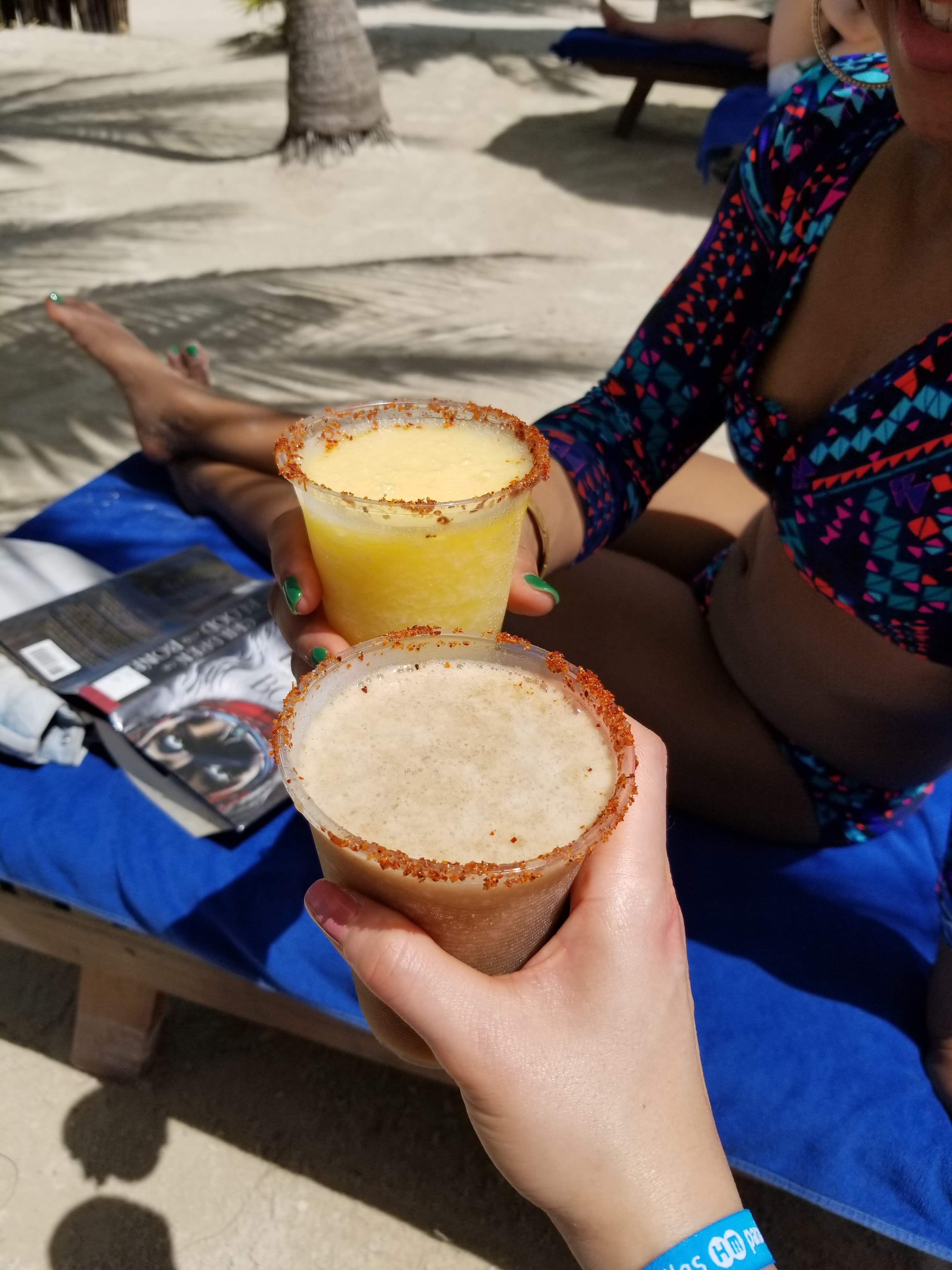 Two beautiful women are holding margaritas in plastic cups - one is a mango margarita the other is a tamarind margarita. In the background is the book Children of Blood and Bone.